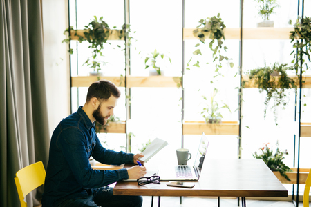 Freelance man working on line with a laptop and holding documents in a coffee shopの写真素材