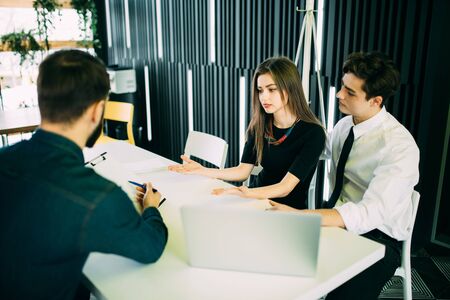 Broker making a presentation to couple showing them a document which they are viewing with serious...
