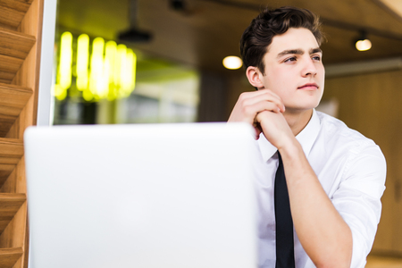 Shot of young man sitting at table looking away and thinking. Thoughtful businessman sitting home office.の写真素材