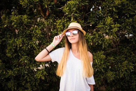 Woman smiling while leaning on wall outdoors ,happy stylish woman hipster standing at green leaves wall, summer travel concept.の写真素材