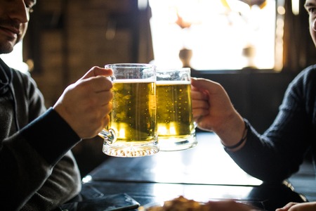 people, leisure and drinks concept - close up of male hands clinking beer glasses and pretzels at bar or pubの写真素材