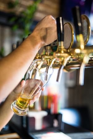 Mans hand pouring pint of beer behind the barの写真素材