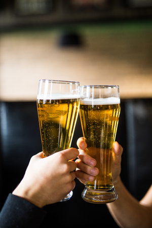 Close-up of two men in shirts toasting with beer at the bar counterの写真素材