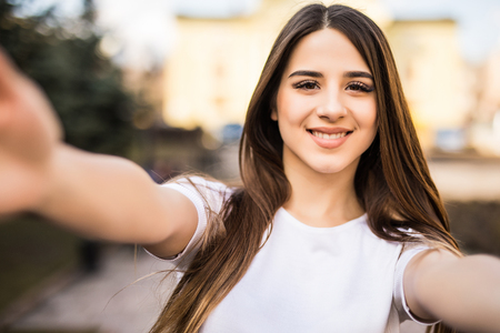 Young woman taking selfie from hands with mobile phone in sunny city street.の写真素材