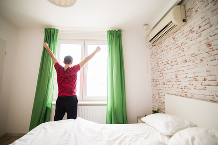 Rear view of a young man waking up in bed and stretching his armsの写真素材