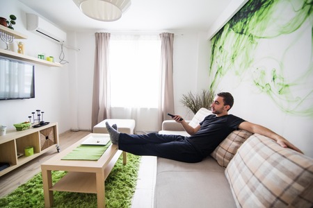 handsome man watching TV on a sofa at homeの写真素材