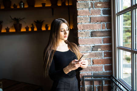 Portrait of a cheerful woman holding smartphone and looking at window