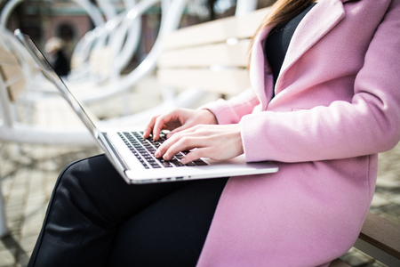 Woman sitting on bench outside and working on computerの写真素材