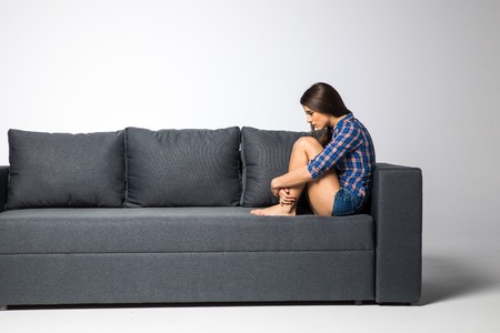 Sad depressed woman at home, she is sitting on the couch lonelinessの写真素材