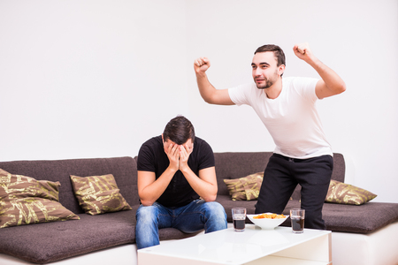 friendship, sports and entertainment concept - happy male friends supporting football team at home. One man happy, another sad.の写真素材