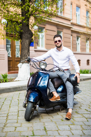 Cheerful young man in helmet is riding on scooter in town.の写真素材