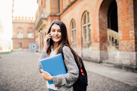 student walking and speak mobile phone with a university building in the backgroundの写真素材