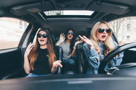 Beautiful girls are sitting with open mouth while having shock during the car drivingの写真素材