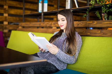 picture of smiling young woman reading book in cafe or work placeの写真素材