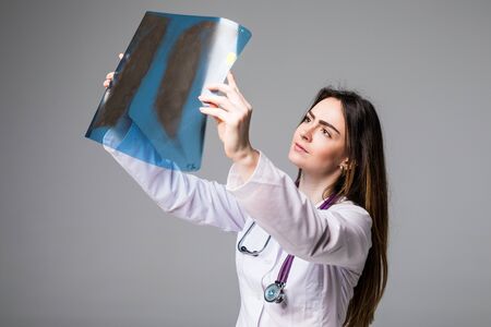 Female doctor examining an x-ray image. Focus is on the x-ray image. Isolated on grey background.