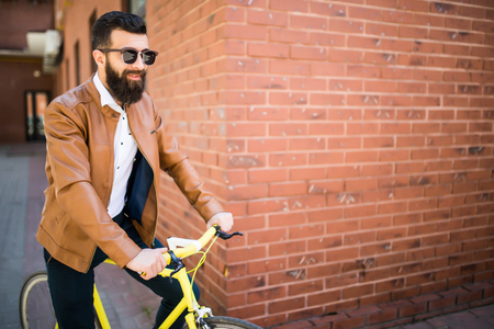 Handsome bearded man while standing near his bicycle against the brick wallの写真素材