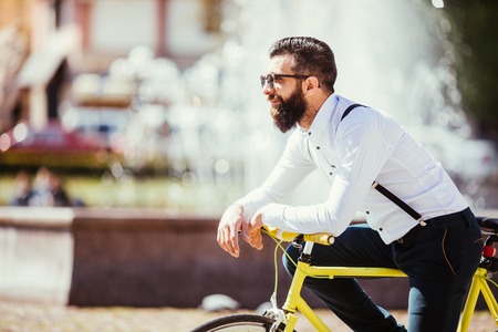 Portrait of handsome young bearded man leaning at his bicycle while standing outdoorsの写真素材