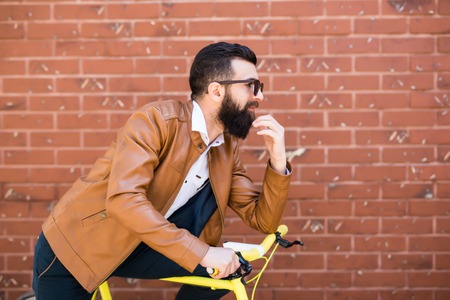 Young handsome man with a beard against the backdrop of a brick wall sits on a bicycle