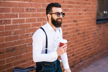 Young bearded man drinking coffee while sitting on his bicycle outdoorsの写真素材