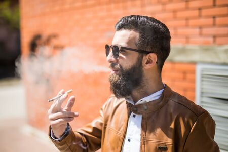 Casual man outdoors smoke a cigarette against brick wallの写真素材