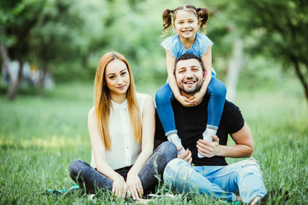 Happy mother, father and daughter in the park. Beauty nature scene with family outdoor lifestyle. Happy family resting together on the grass, having fun outdoor. Happiness and harmony in family life.の写真素材
