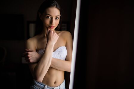 Beautiful woman opening curtains and looking through the windowの写真素材