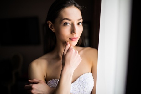 Beautiful woman opening curtains and looking through the windowの写真素材