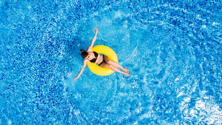 Top view of slim young woman in bikini on the yellow air inflatable ring in the big swimming pool.の写真素材