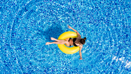 Aerial view of young brunette woman swimming on the inflatable big yellpw in the pool. Top view of slim lady relaxing on her holidays.の写真素材