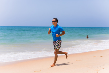 Man running on tropical beach at sunsetの写真素材