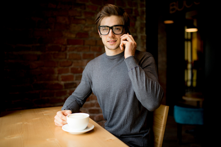 Young happy manager talking on phone and drinking coffeeの写真素材