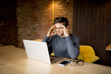 Handsome man working at laptop with sad face or head ache  working at laptop