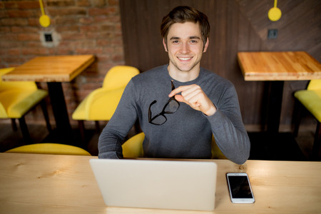 Handsome and relaxed man sitting at a cafe table outside working remote with his laptopの写真素材