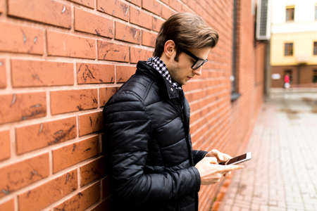 Typing text message side view of handsome young man in smart casual wear holding mobile phone brickの写真素材