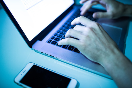 Close up of male hands typing on keyboard with white screen in the night. Hackerの写真素材