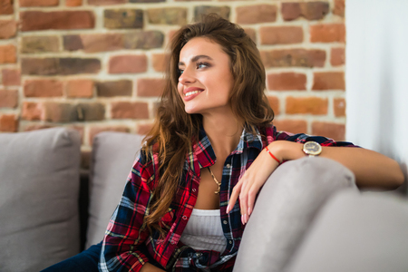 Smiling beautiful brunette relaxing on the couch and looking at camera in the living room at homeの写真素材