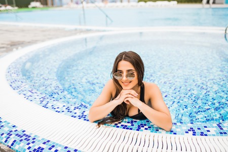 beautiful woman in a hat sitting on the edge of the pool