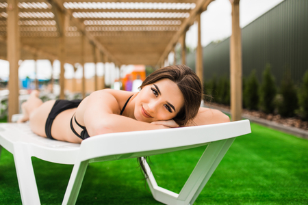 Young woman in bikini, hat and swimsuit laying on chaise-longue and sunbathing by the pool in a summer vacationの写真素材