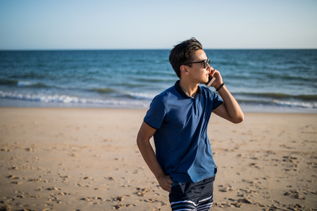 Young asian man  talking on phone and see the sunset on tropical beachの写真素材