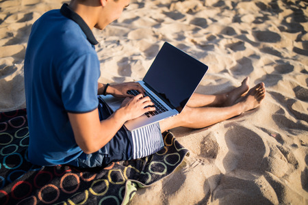 Young asian man working with laptop computer on tropical beachの写真素材