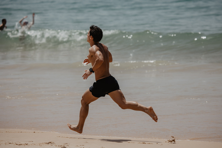 Young Man In Fitness Clothing Running Along Beachの写真素材