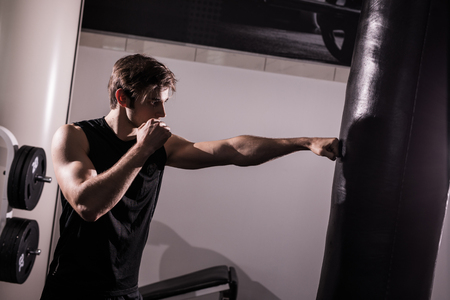 Concentrated muscular kickbox fighter exercising with punch bag on whiteの写真素材