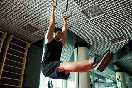 Fitness handsome man doing dipping exercise using rings in the gym