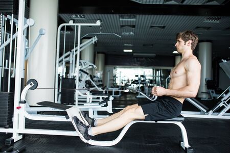 Brutal athletic man pumping up muscles on crossover. Muscular man working out in gym doing exercises...
