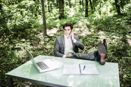Relaxed business man in suit in green park at office desk talk at mobile phone. Business concept.の写真素材