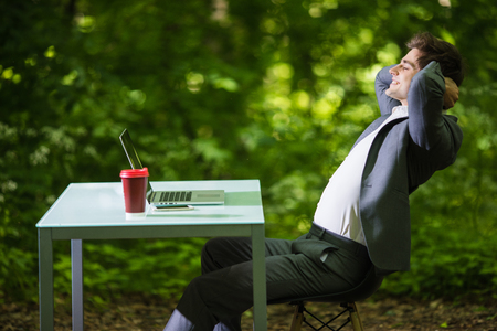 Side portrait of business man working at laptop on office desk in green park. Business conceptの写真素材