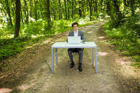 Portrait of Businessman sitting at the office desk work at laptop computer in green forest park. Freelancer working on office table in green park.の写真素材