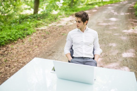 Confident business man sitting at office desk on road of green forest.の写真素材