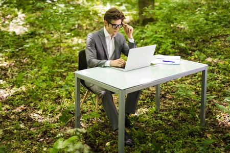 Handsome business man working at laptop at office table in green park. Business concept.の写真素材