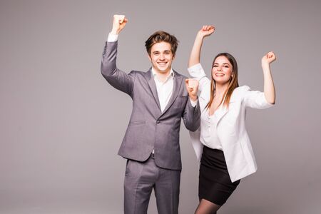Concept of partnership in business. Young man and woman standing with raised hands against gray backgroundの写真素材